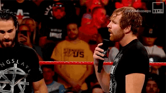 a wrestler is talking into a microphone while another wrestler looks on