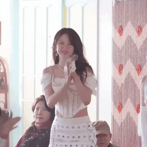 a woman in a white dress is standing in front of a group of people and clapping .