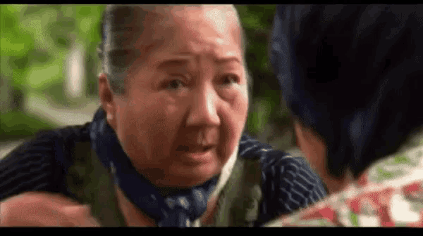 an elderly woman is talking to a younger woman while wearing a scarf around her neck .