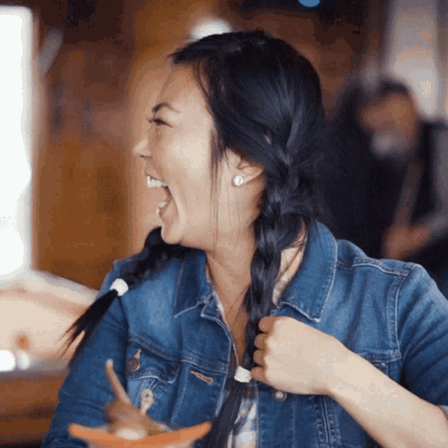 a woman in a denim jacket is laughing and holding her hair