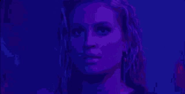 a close up of a woman 's face in a dark room with purple lights .