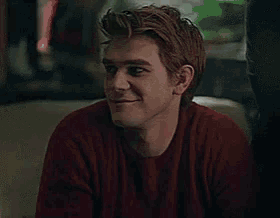 a woman wearing a grey sweater and a white collar is smiling and looking at the camera .