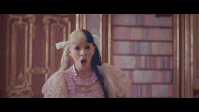 a little girl in a pink dress with a bow in her hair is making a surprised face .