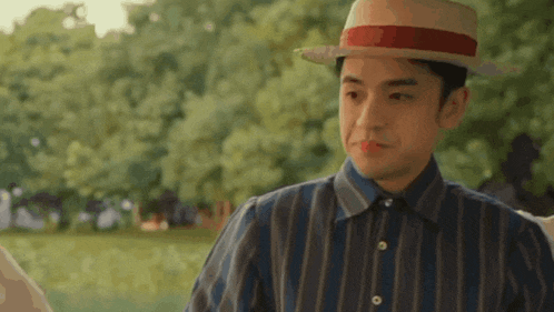 a man wearing a hat and a striped shirt is standing in a field .