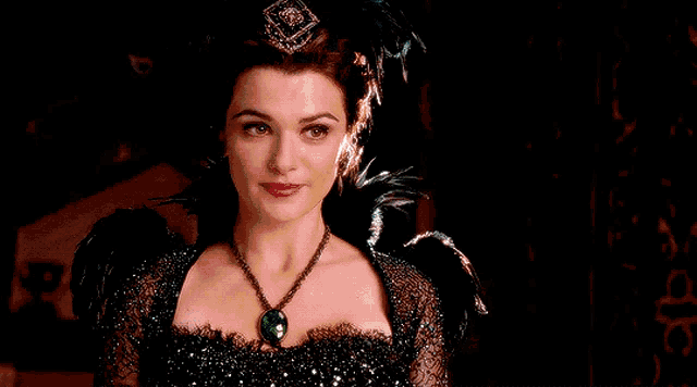a woman wearing a black dress and a green necklace looks at the camera