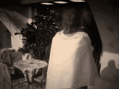a black and white photo of a woman standing in front of a table .