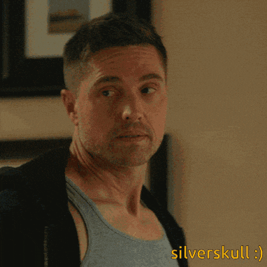 a man wearing a blue tank top and a black jacket is standing in front of a wall that says silverskull on it