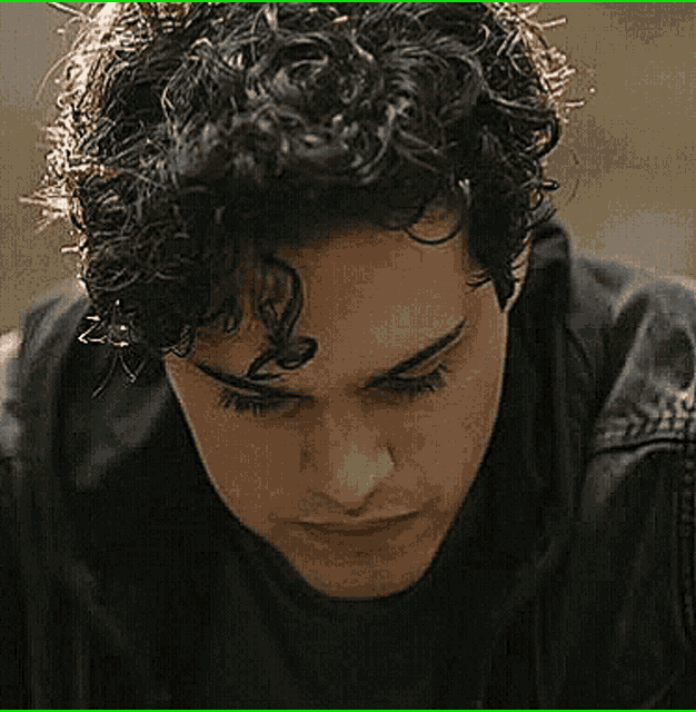 a close up of a man 's face with curly hair and a black jacket .