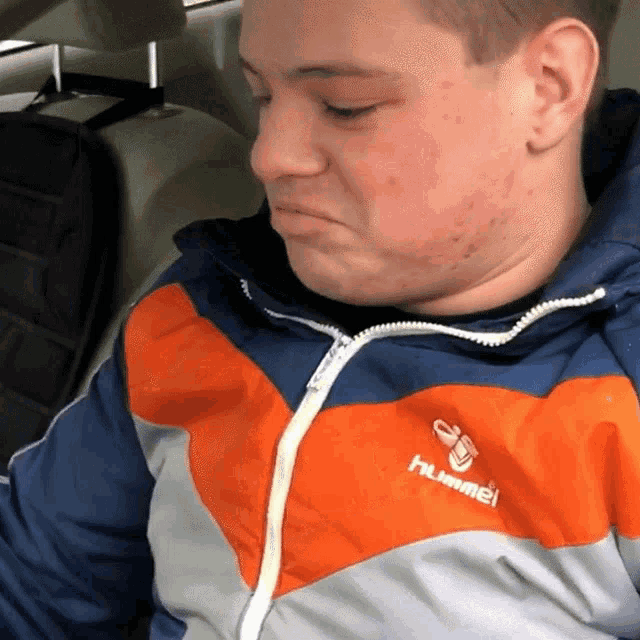 a man wearing an orange and blue hummel jacket looks down