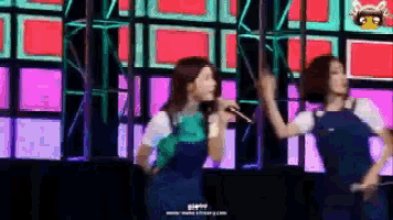 two women are dancing on a stage with a microphone .