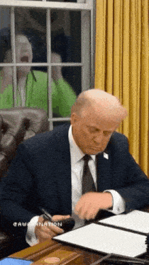 a man in a suit and tie sits at a desk with a pen in his hand
