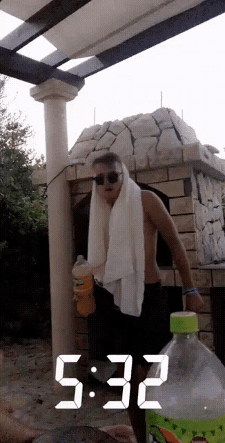 a man with a towel around his neck is drinking from a bottle and the time reads 5:33