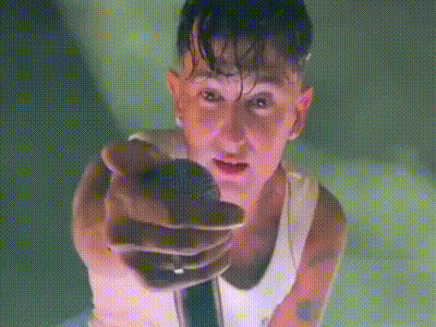 a man in a white tank top is holding a microphone and pointing at the camera