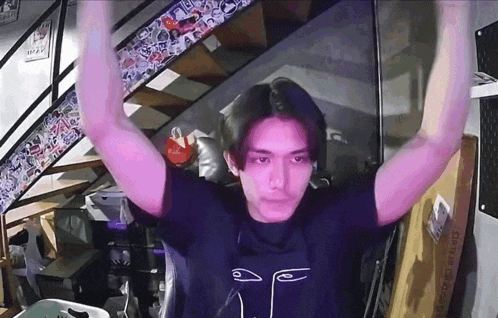a man wearing a black shirt with a face on it holds his arms up in the air