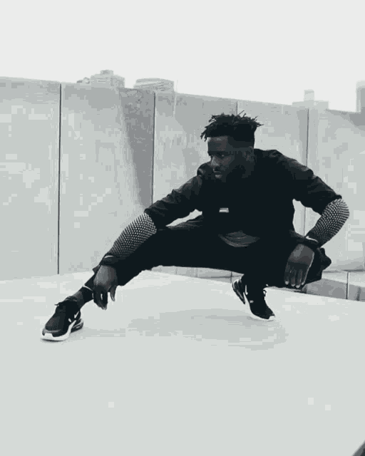 a man wearing a black jacket and black pants is squatting down