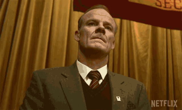 a man in a suit and tie stands in front of a banner that says netflix