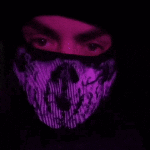a man wearing a purple mask with a skull on it is standing in the dark .