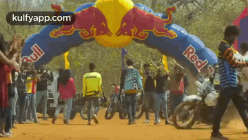 a group of people are walking under a red bull inflatable archway .
