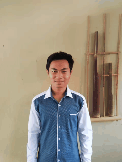 a young man wearing a blue and white shirt stands in front of a wall