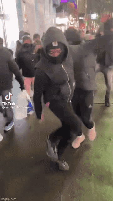 a man wearing a mask and a hoodie is dancing on the street .