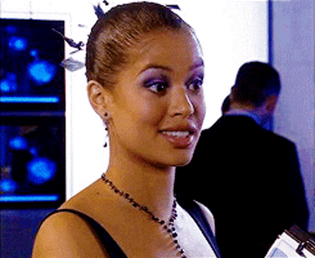 a woman wearing a black dress and a necklace smiles for the camera