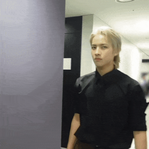 a young man in a black shirt and tie stands in a hallway
