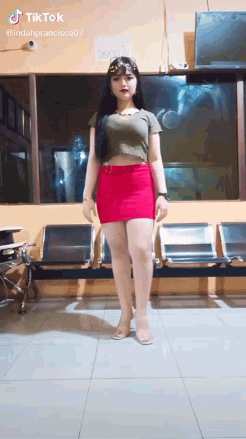 a woman in a red skirt and crop top is standing in a room with chairs .