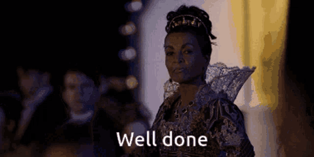 a woman in a fancy dress is standing in front of a crowd and says well done .