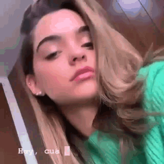 a woman wearing a green sweater is taking a selfie with her hair blowing in the wind .