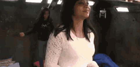 a woman in a white lace top is standing in a dark room with a woman in a black shirt behind her .