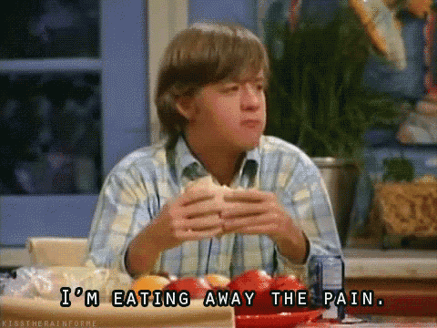 a man is sitting at a table eating a sandwich and saying i 'm eating away the pain
