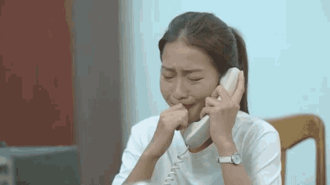 a young woman is crying while talking on a telephone .