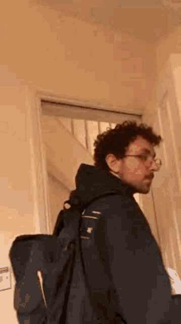 a man wearing glasses and a backpack is standing in a hallway .