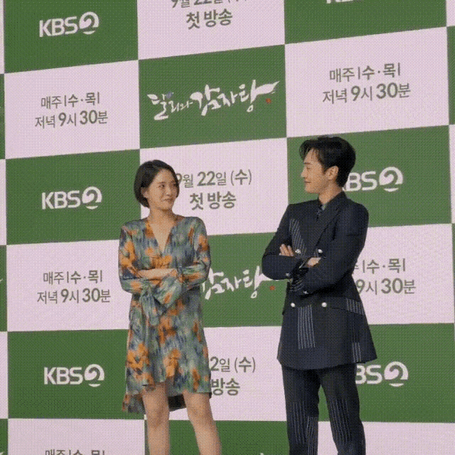 a man and a woman are standing in front of a wall that says kbs2