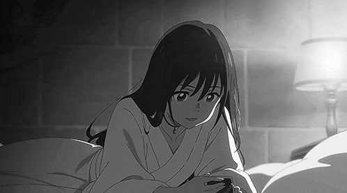 a black and white photo of a girl laying on a bed with a lamp in the background .