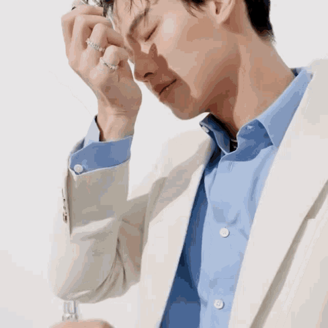 a man wearing a white jacket and a blue shirt has his eyes closed