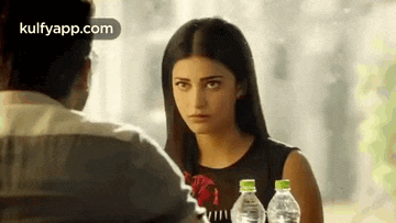 a man and a woman are sitting at a table with bottles of water and looking at each other .