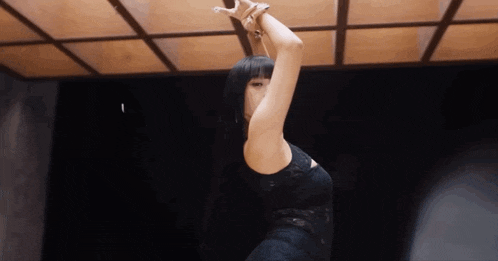 a woman in a black dress is dancing in a dark room with a wooden ceiling