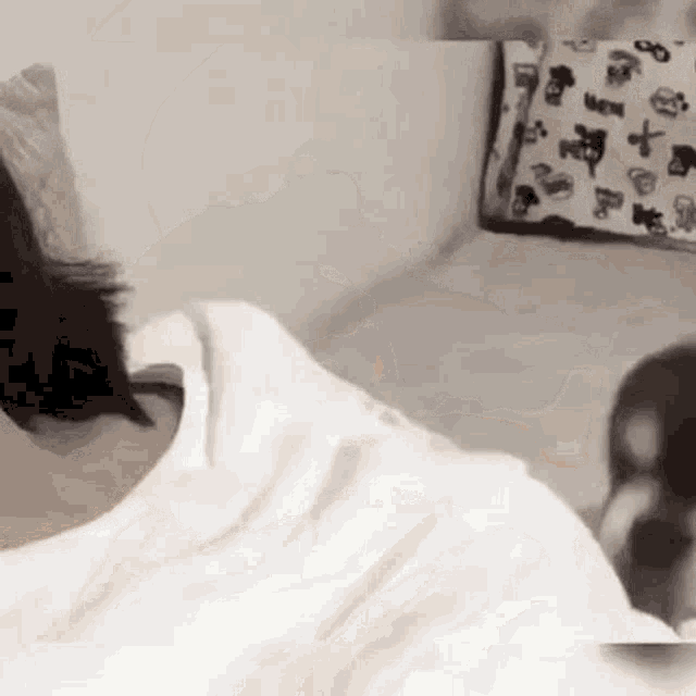 a person is laying on a bed with a white shirt on and a pillow on the wall .