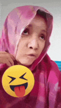 a woman wearing a pink hijab holds a yellow smiley face with a tongue sticking out