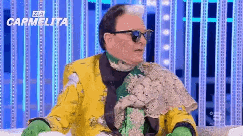 a man in a yellow jacket and green gloves is sitting on a couch with the word carmelita behind him