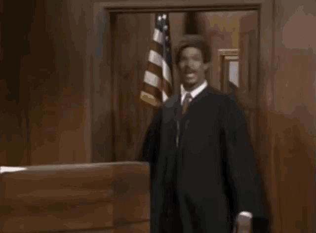 a man in a judge 's robe is standing in front of a door that says hey mon