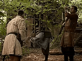 a group of men are standing in a forest holding swords