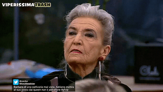 an older woman with gray hair is sitting in front of a sign that reads viperissima trash