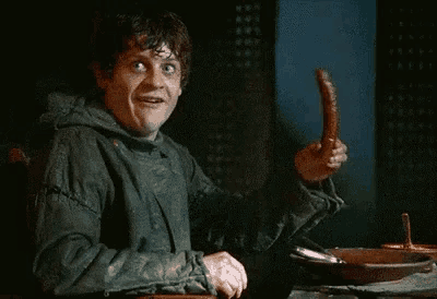 a man is sitting at a table holding a sausage and smiling