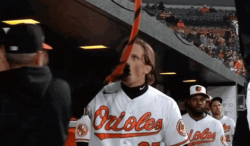 a man wearing a orioles jersey holds a bat in his mouth