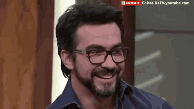a man with glasses and a beard is smiling in front of a sign that says " coisas datvyoutube.com "