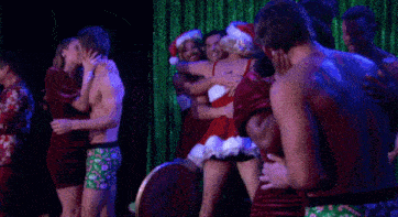a group of people are hugging in front of a green curtain and one of them is wearing a santa hat