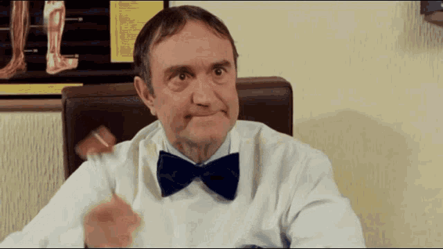 a man in a white coat and blue bow tie is sitting in front of a poster of a foot