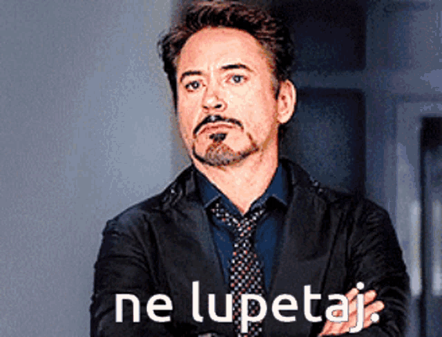 a man with a beard and mustache is standing with his arms crossed in front of a sign that says ne lupetaj